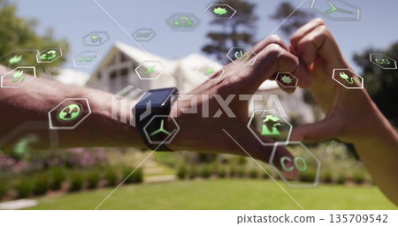 Forming heart shape with couple's hands in front yard, with smartwatch and renewable energy icons Forming heart shape with couple's hands in front yard, with smartwatch and renewable energy icons 135709542