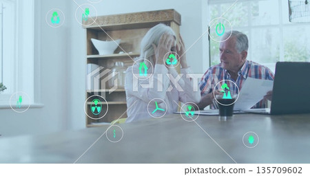 Examining bills older man showing papers and woman holding head at kitchen table with energy icons 135709602
