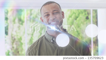 Smiling African American man wearing olive green shirt standing before garden door with lens flare 135709623