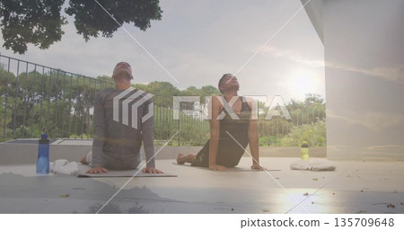 Practicing two men holding upward-facing dog pose on balcony, with yoga mats towels water bottles 135709648