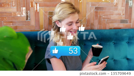 Holding smartphone and mug, woman scrolling notifications in cafe, floating thumbs-up and 53 bubble Holding smartphone and mug, woman scrolling notifications in cafe, floating thumbs-up and 53 bubble 135709649
