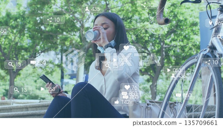 Masked woman sipping coffee holding smartphone on park bench with bicycle, smartwatch, social icons Masked woman sipping coffee holding smartphone on park bench with bicycle, smartwatch, social icons 135709661