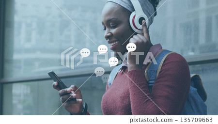 Standing woman adjusting over-ear headphones at transit stop, with phone and backpack, copy space Standing woman adjusting over-ear headphones at transit stop, with phone and backpack, copy space 135709663