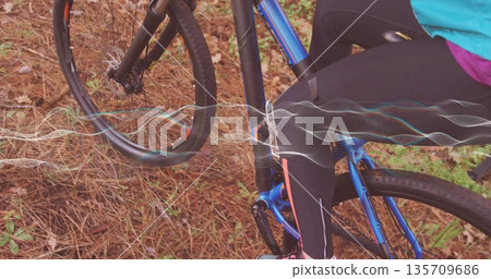 Adult cyclist riding on forest trail in tight athletic wear, with blue bicycle and waveform overlay 135709686