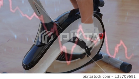 Pressing black-and-white sports shoe onto exercise bike pedal in home gym, red line graph overlay Pressing black-and-white sports shoe onto exercise bike pedal in home gym, red line graph overlay 135709691