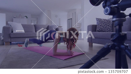 Woman practicing forearm plank on pink yoga mat in modern living room, with DSLR camera 135709707