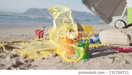 Arranging colorful sand buckets and shovel on sunny beach shore, with striped towel and cooler bag 135709721