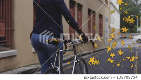 Woman in navy top guiding silver bicycle in narrow street, with crossbody bag and gold stars Woman in navy top guiding silver bicycle in narrow street, with crossbody bag and gold stars 135709754