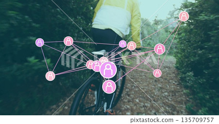 Riding mid-adult cyclist pedaling bicycle through narrow leafy forest trail, with yellow jacket 135709757