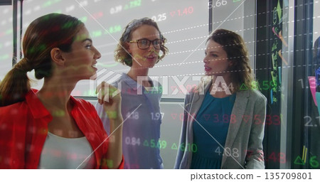 Discussing professional women gesturing at glass board in modern office, with stock data overlay Discussing professional women gesturing at glass board in modern office, with stock data overlay 135709801