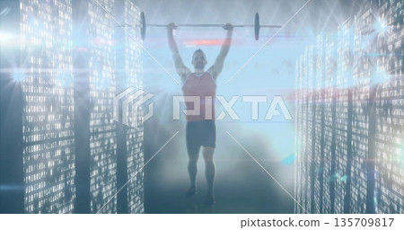Lifting athlete wearing red top, black shorts pressing barbell overhead in code corridor with mist 135709817