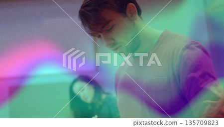 Standing focused male soaking green purple pink light projections in sparse room, with ambient hues Standing focused male soaking green purple pink light projections in sparse room, with ambient hues 135709823