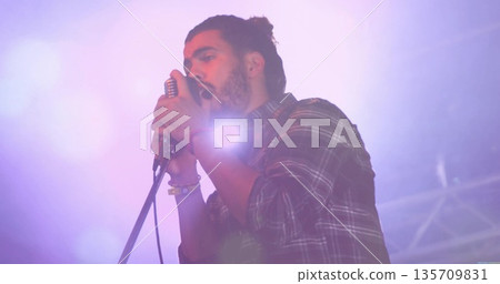 Singing musician in flannel shirt holding vintage mic on stage with colored spotlights and haze Singing musician in flannel shirt holding vintage mic on stage with colored spotlights and haze 135709831