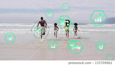 Running family of four splashing into surf at sandy beach, with green hexagonal icons 135709902