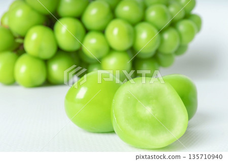Close-up of fresh green seedless grapes, varieties shine muscat, with sliced pieces on a white background 135710940