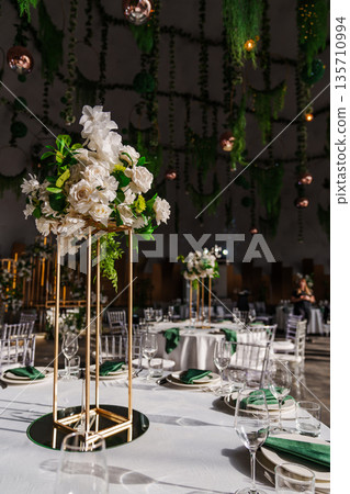 flower arrangements, empty glasses, plates with green napkins on a table. 135710994