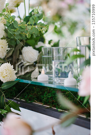 Small electronic candles in floral decor on the banquet table. Small electronic candles in floral decor on the banquet table. 135710999