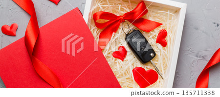 Black car key in a present box with a ribbon and red heart on colored background. Valentine day composition Top view Black car key in a present box with a ribbon and red heart on colored background. Valentine day composition Top view 135711338