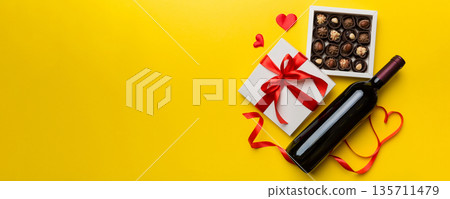 Bottle of red wine on colored background for Valentine Day with gift and chocolate. Heart shaped with gift box of chocolates top view with copy space Bottle of red wine on colored background for Valentine Day with gift and chocolate. Heart shaped with gift box of chocolates top view with copy space 135711479
