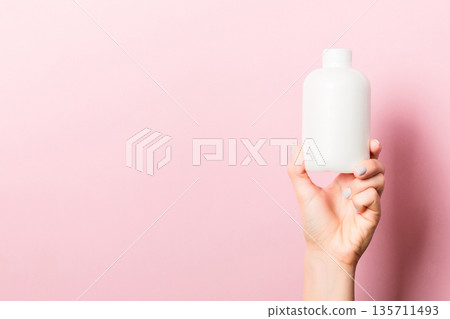 Female hand holding cream bottle of lotion isolated. Girl give tube cosmetic products on pink background 135711493