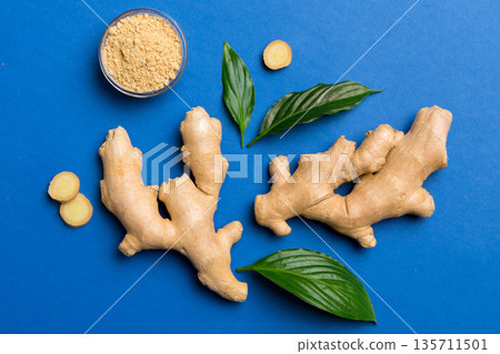 Finely dry Ginger powder in bowl with green leaves isolated on colored background. top view flat lay Finely dry Ginger powder in bowl with green leaves isolated on colored background. top view flat lay 135711501