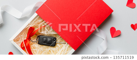 Black car key in a present box with a ribbon and red heart on colored background. Valentine day composition Top view Black car key in a present box with a ribbon and red heart on colored background. Valentine day composition Top view 135711519