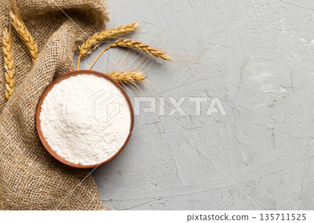 Flat lay of Wheat flour in wooden bowl with wheat spikelets on colored background. world wheat crisis Flat lay of Wheat flour in wooden bowl with wheat spikelets on colored background. world wheat crisis 135711525