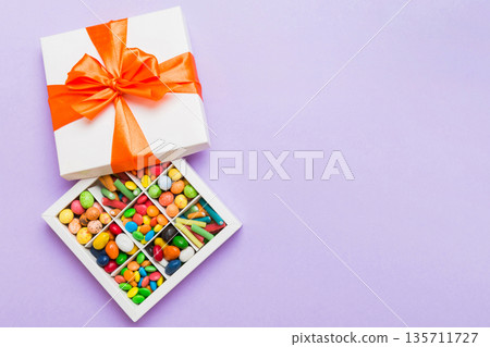Set of different sweet candy in a paper box with a satin ribbon on a colored background. Holiday concept 135711727