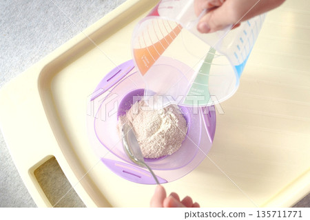 baby food and nutrition concept - mother hands with jar, spoon and bowl preparing cereal from powder close up baby food and nutrition concept - mother hands with jar, spoon and bowl preparing cereal from powder close up 135711771