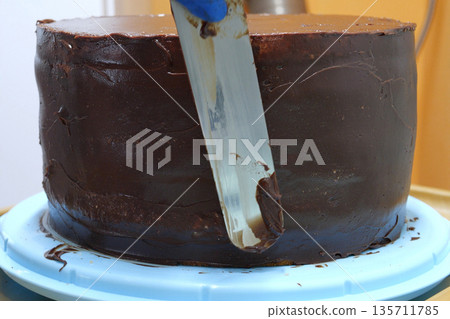 Confectioner woman is smearing cream on sides of cake using spatula, closeup view. culinary, baking and cooking food concept, home cooking Confectioner woman is smearing cream on sides of cake using spatula, closeup view. culinary, baking and cooking food concept, home cooking 135711785