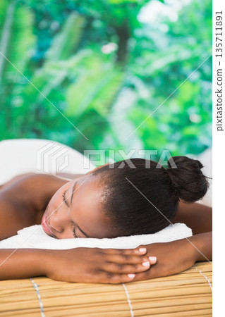 African American woman lying face down on massage table in spa relaxing with white spa linens African American woman lying face down on massage table in spa relaxing with white spa linens 135711891