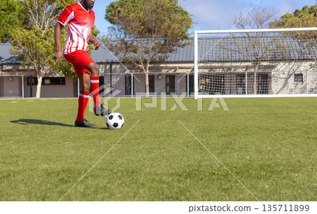 African American man controlling soccer ball near goalpost on turf in red uniform, copy space 135711899