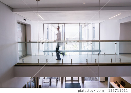 Glass-paneled walkway spanning upper corridor overlooking lobby below with pendant light above 135711911