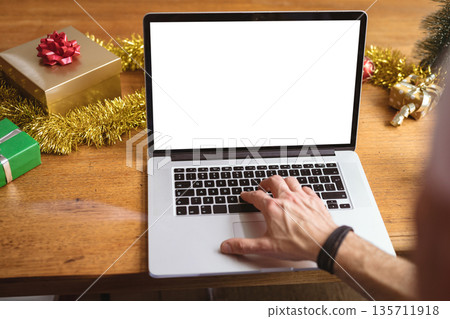 Man reaching toward silver laptop on festive table at home with gift boxes and tinsel garland 135711918