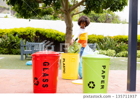African American child lowering bag into yellow bin among glass, paper bins on brick pavement African American child lowering bag into yellow bin among glass, paper bins on brick pavement 135711937