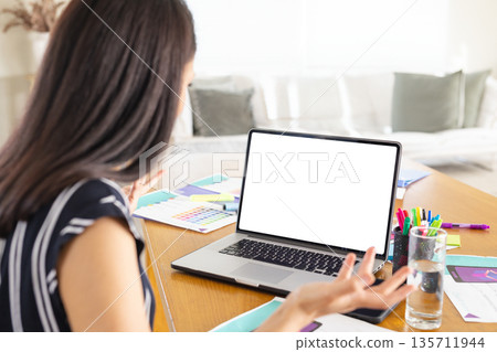 Asian woman working at wooden table in home living room with laptop, swatches, design layouts Asian woman working at wooden table in home living room with laptop, swatches, design layouts 135711944