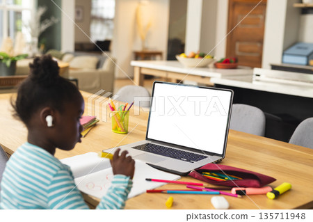 African American child sitting at home concentrating on schoolwork with notebook, pencil and laptop African American child sitting at home concentrating on schoolwork with notebook, pencil and laptop 135711948