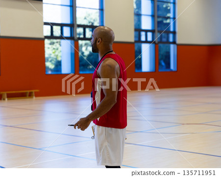 African American male sports coach standing on court in gym holding timer wearing whistle lanyard African American male sports coach standing on court in gym holding timer wearing whistle lanyard 135711951