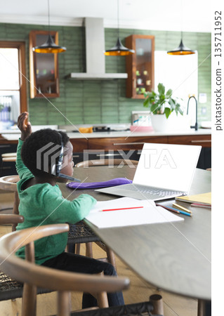 African American boy studying using laptop with headset at dining table in kitchen, copy space African American boy studying using laptop with headset at dining table in kitchen, copy space 135711952