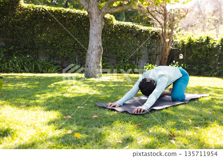 Woman practicing child's pose on yoga mat in garden wearing athletic top with leggings, copy space Woman practicing child's pose on yoga mat in garden wearing athletic top with leggings, copy space 135711954