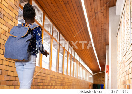 African American child walking down school hall with denim backpack near windows and recycling bins African American child walking down school hall with denim backpack near windows and recycling bins 135711962