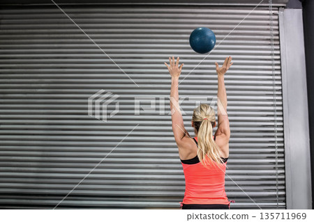 Athletic woman performing overhead throw with dark blue medicine ball in industrial gym, copy space Athletic woman performing overhead throw with dark blue medicine ball in industrial gym, copy space 135711969
