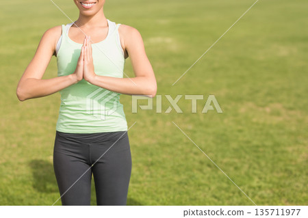 White woman standing in park holding hands together in yoga prayer pose wearing athletic clothing 135711977