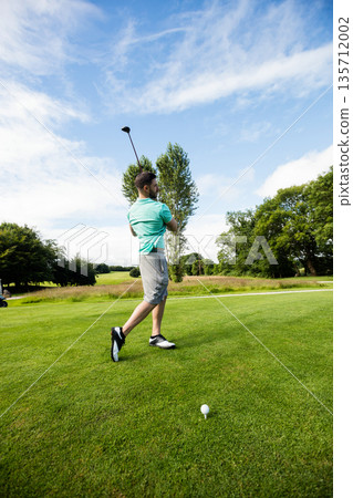 Male golfer striking ball on golf tee beside white tee marker wearing teal polo shirt Male golfer striking ball on golf tee beside white tee marker wearing teal polo shirt 135712002