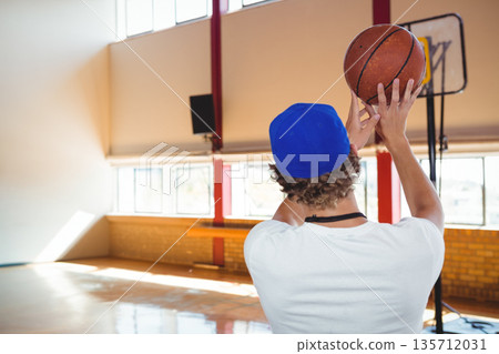 Teen boy holding basketball overhead and preparing shot on gym court with portable hoop 135712031