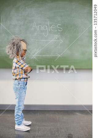 African American boy wearing gray wig crossing arms facing classroom chalkboard angle, copy space African American boy wearing gray wig crossing arms facing classroom chalkboard angle, copy space 135712049