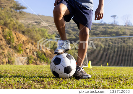 African American boy balancing on soccer ball wearing cleats on field by goal net and cones 135712063