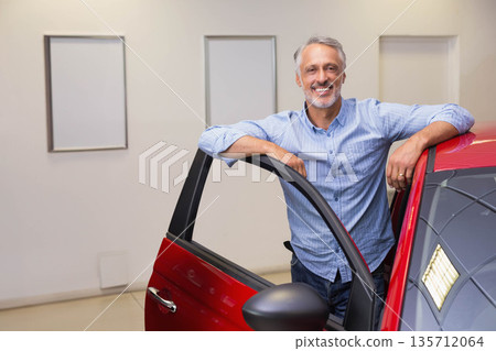 Man leaning against open driver door of red car in showroom highlighting ring and light reflection Man leaning against open driver door of red car in showroom highlighting ring and light reflection 135712064