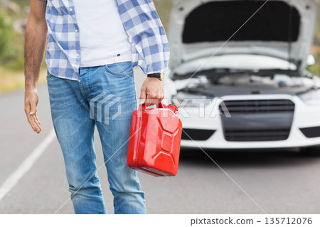 Mid adult male holding red fuel container beside white sedan with open hood on rural road Mid adult male holding red fuel container beside white sedan with open hood on rural road 135712076