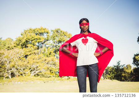 African American woman posing in park wearing red superhero cape, mask, wristbands and heart tee African American woman posing in park wearing red superhero cape, mask, wristbands and heart tee 135712136